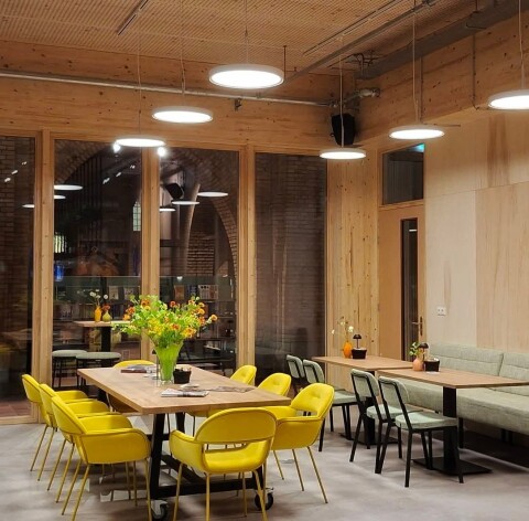 De Foyer, 2 gezellige tafels met gele stoelen. Op de tafels staan mooie bloemen